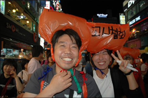 촛불문화제에 참석한 시민들이 쓰레기 봉투에 구호를 적어 머리에 모자처럼 쓰고 있다.