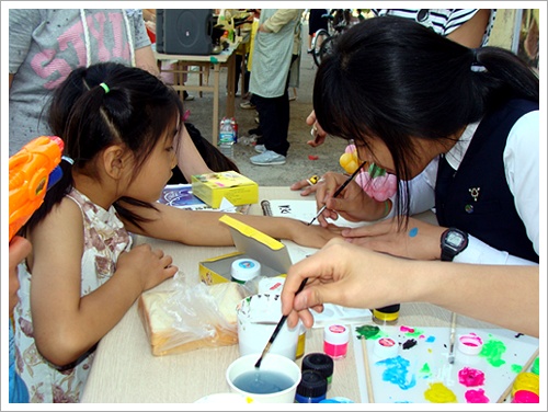 초등학생의 팔에 예쁜 꽃을 그려주고 있는 서울여상 자원봉사자