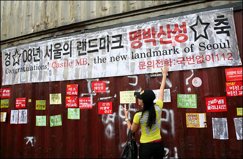 10일 오후 경찰이 설치한 '콘테이너 장벽'에 촛불집회 참가자들이 '경축 08년 서울의 랜드마크 명박산성' 이라고 적힌 현수막과 집회 구호가 적힌 피켓을 붙였다. 그 앞에서 기념촬영을 하고 있는 한 시민.