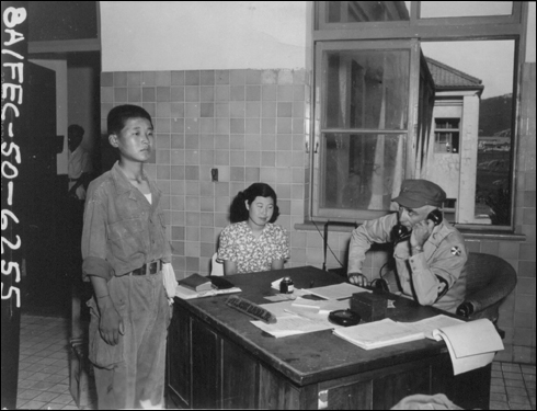 인민군 소년병이 포로로 붙잡혀 미 조사관에게 심문을 받고 있다. 가운데 여인은 통역이다(1950. 8. 18.).