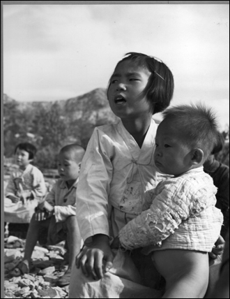 엄마는 일터로 가고 소녀는 동생을 데리고 노천교실에서 수업을 받고 있다(1950. 10. 서울 은평).