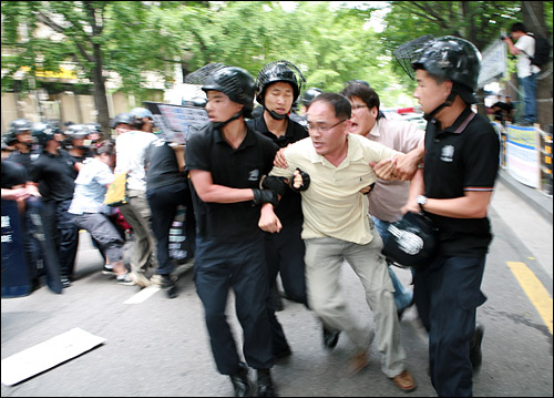 26일 오전 서울 세종문화회관 앞에서 정부의 미국 쇠고기 수입 위생 조건 고시 강행 철회를 요구하는 집회를 연 시민사회단체들이 청와대로 향하기 위해 정부중앙청사 후문길로 뛰어가다가 경찰에 의해 제지당하고 있다.