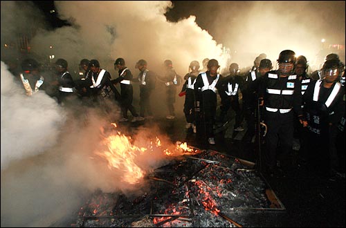 27일 새벽 미국산쇠고기 장관고시 무효와 재협상을 촉구하며 밤샘시위를 벌이던 시민들을 경찰이 강제해산 시키고 있다. 살수차에 젖은 옷을 말리기 위해 시민들이 불을 피워 놓은 곳을 경찰들이 지나고 있다.