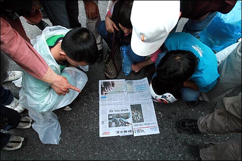 27일 새벽 미국산쇠고기 장관고시 무효와 재협상을 촉구하며 밤샘시위를 벌였던 시민들이 조선일보와 서울신문을 나란히 놓고 시위 상황을 다룬 기사를 살펴보고 있다.