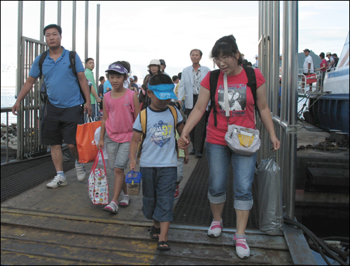 쾌속선에서 내려 부잔교 위를 걸어나오고 있는 지오네 가족. 배낭 하나씩 메고 손에도 짐 하나씩 들고 있다.