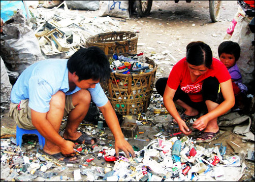 가족이 전자쓰레기 처리작업을 하고 있는 가운데, 아이가 두려운 눈빛으로 쳐다보고 있다.
