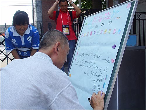  자원봉사자들이 마련한 올림픽의 성공적 개최 기원란에 글을 적어 넣고 있는 베이징시민의 모습이다.