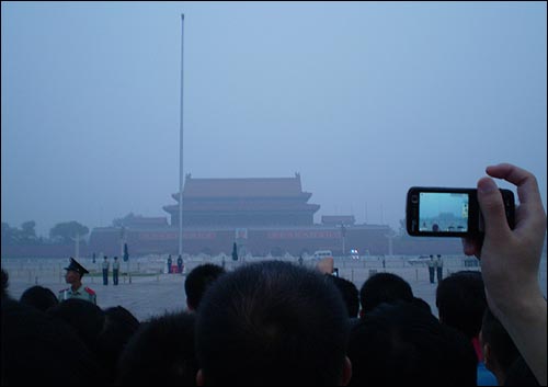  오성홍기 게양식을 보러온 사람들이 손에 든 소형카메라에 게양 장면을 담고 있다.