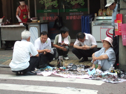 시장 사람들. 바닥에 자판을 벌여놓은 아줌마와 그 주위를 둘러싸고 이야기를 나누는 사람들.