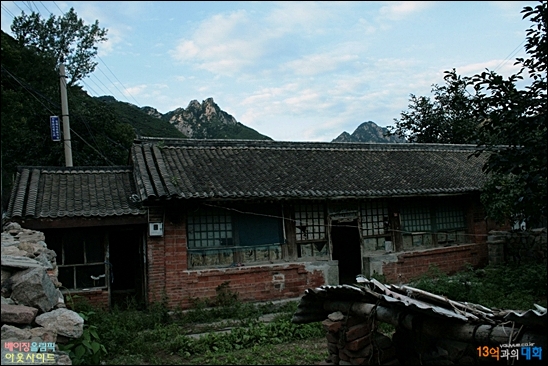 시자즈 부근 톈펑룽칭 마을의 허름한 집, 돌담이 있고 뒤편으로 장성이 보이는 산이 보인다