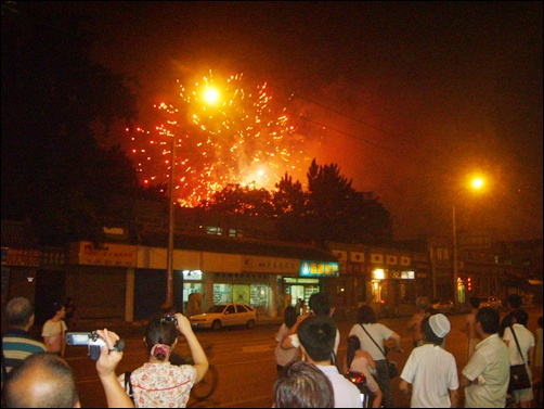  베이징 올림픽 마지막날, 시민들이 거리에서 불꽃놀이를 감상하고 있다.
