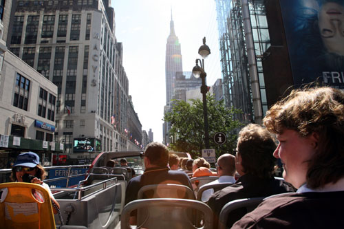 이층버스를 타고 시내 관광을 하는 관광객들의 정면에 뉴욕의 상징인 엠파이어 스테이트 빌딩이 보인다