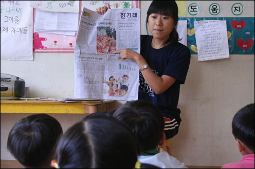 한 선생님이 신문을 보여주며 멜라민이 검출돼 폐기처분 되는 과자에 대하여 아이들에게 설명하고 있다.