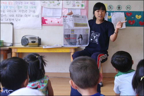  선생님이 경남도민일보를 보여주며, "과자 사먹기 겁난다. 멜라민 공포, 손길 뚝"이라고 되어 있는 기사를 아이들에게 설명해주고 있다.