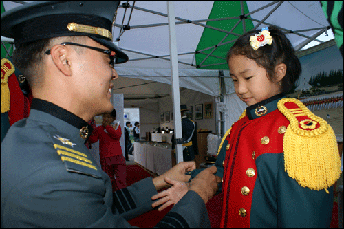 한 어린 꼬마가 기념촬영을 위해 육군 3사관학교 한 생도의 도움을 받으며 제복을 입고 있다.