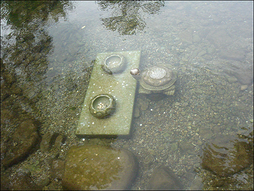 돌다리 옆에는 목만 살짝 내민 거북이 한 마리와 동전이 여기저기 떨어져 있는 사각 진 돌 받침대 위에 동그란 그릇 두 개가 물에 잠겨 있다

