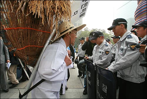 벼를 담은 지게를 진 농민의 행진을 경찰들이 가로막고 있다.