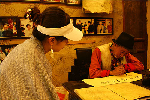 한 여성 관광객이 산 전통종이에 동파문자를 써주는 동파. 동파교의 사제였던 동파는 오늘날 종이공방에 고용되어 동파문자를 써주며 살아가고 있다.