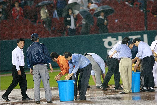  23일 저녁 서울 잠실야구장에서 열린 2008 프로야구 플레이오프 6차전 두산-삼성 경기에서 3회말 갑자기 내린 폭우로 경기가 중단되어 두산 관계자들이 경기장에 나와 그라운드의 물을 제거하고 있다.
