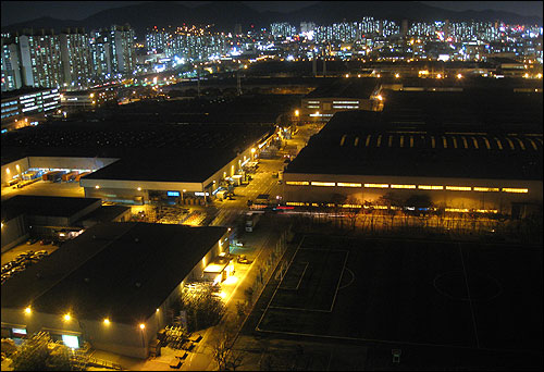 18일 저녁, 잔업이 사라진 인천 부평구 청천동 GM대우 부평공장을 인근 아파트에서 바라본 모습. 공장의 모습이 불빛을 내뿜고 있는 주변 아파트와 달리 매우 어두운 모습이다.