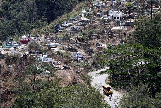 마우비시에서 수아이 가는 구불구불한 도로를 트럭과 오토바이가 달리고 있다. 위쪽은 마우비시 공동묘지.