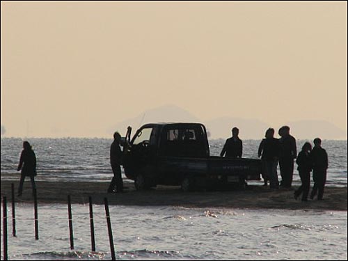 주변에 있던 사람들이 바닷물에 빠진 트럭을 빼내고 있다.
