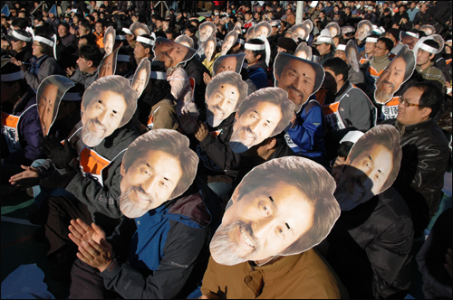 14일 사천에서 열린 '진보 희망 지키기 촛불문화제'에 참석한 사람들이 강기갑 의원을 얼굴 모양인 가면을 쓰고 앉아 있다.