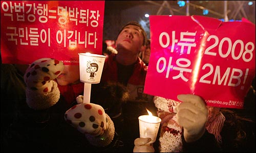 1일 새벽 서울 종로 보신각에서 2009년 새해를 알리는 타종식이 열리는 가운데, 이명박 정권을 규탄하는 피켓과 촛불을 든 시민들이 '이명박 퇴진'을 외치고 있다.