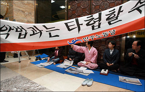 민주당이 국회 로텐더홀에서의 농성을 해제한 5일 오전 강기갑 대표 등 민주노동당 의원들이 본회의장 출입문에 쇠사슬로 몸을 묶은 채 단독 농성에 들어가기 앞서 'MB악법과는 타협할 수 없다'고 적힌 대형 플래카드를 내걸고 있다.