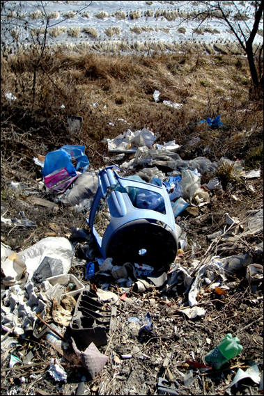 도로 너머 쓰레기들은 논과 농수로를 오염시킨다.