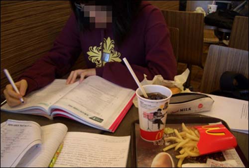 한 여중생이 햄버거 세트를 옆에 놓고 학원 숙제를 하고 있다. 