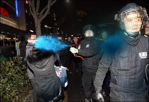 경찰이 한 여성의 얼굴을 향해 색소를 발사하고 있다.