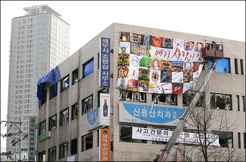 철거민 5명과 경찰특공대 1명이 사망한 '용산철거민참사' 한달을 맞은 20일 오후 서울 용산구 한강로 2가 남일당건물에 '여기 사람이 있다'는 글과 철거민들의 모습을 담은 대형 걸개그림이 걸리고 있다.