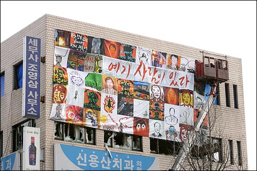 철거민 5명과 경찰특공대 1명이 사망한 '용산철거민참사' 한달을 맞은 2월 20일 오후 서울 용산구 한강로 2가 남일당건물에 '여기 사람이 있다'는 글과 철거민들의 모습을 담은 대형 걸개그림이 걸리고 있다.