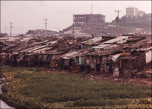  1970년대 청계천 하류 일대는 무허가 판자집 집성촌이었다. 그 뒤로 새로 짓는 건물들이 보인다. 박정희가 추진한 산업화, 근대화의 일그러진 모습이다. 이 사진은 당시 구호 활동을 했던 일본인 목사 노무라 모토유키가 찍어 한국 정부에 기증한 것의 일부다.