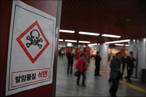 부산석면추방공동대책위가 부산지하철 서면역 벽몉에 석면의 위험을 경고하는 딱지를 붙여 놓은 가운데, 시민들이 그 앞을 지나고 있다.