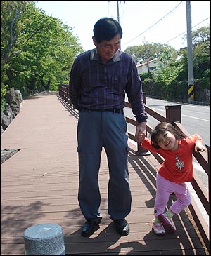 할아버지와 다섯 살 된 손녀가 손을 잡고 길을 걷는다. 60년 전과 후, 이들이 생각하는 고향은?