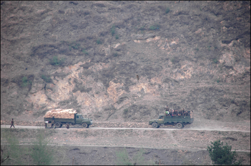 북한 양강도 중부 압록강 연안에 있는 혜산시에 붙은 도로에 트럭 두 대가 지나가고 있다. 트럭 한 대는 짐을 가득 실었고, 반대편 트럭은 사람을 짐칸에 태웠다.