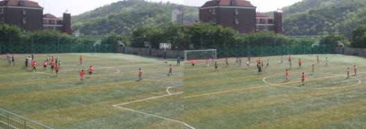 남강 중학교의 인조잔디 축구장에서 운동하는 학생들. 주변에는 푸른 나무들이 있으니, 후배들은 쾌적한 환경에서 축구를 즐겁게 할 수 있었습니다.