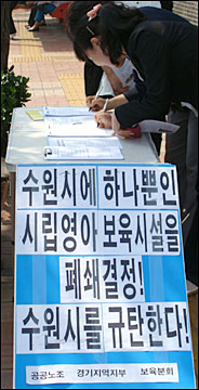 수원시청 앞에 설치된 어린이집 폐쇄 철회를 위한 서명대에서 시민들이 서명하고 있다.