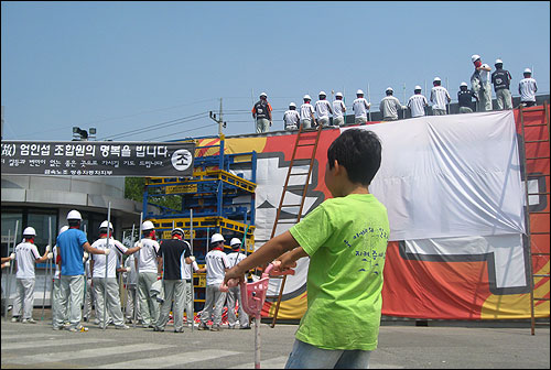 2009년 6월 쌍용차 평택공장에서 쌍용차 노동자들의 공권력 침탈 대비 훈련을 한 노동자의 아들이 지켜보고 있다.
