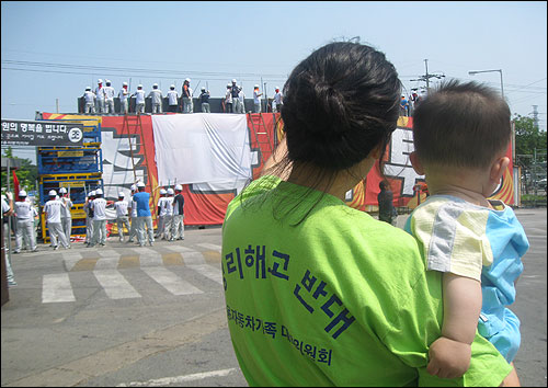 2009년 6월 5일 오후 쌍용차 평택공장 앞의 모습이다. 아이를 안은 어머니가 해고 노동자들의 공권력 침탈 대비 훈련 모습을 걱정스러운 듯 지켜보고 있다. 