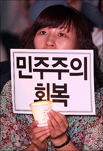 10일 저녁 서울 시청앞 서울광장에서 열린 '6월항쟁 계승 및 민주회복 범국민대회'에 참석한  한 시민이 '민주주의 회복'이 적힌 손피켓과 촛불을 들어보이고 있다.