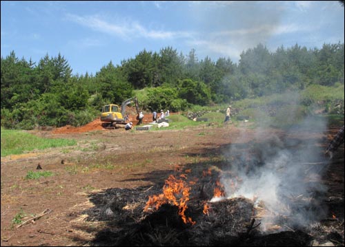 해체된 초분에서 나온 이엉은 불에 태워지고, 저만치에선 포클레인을 동원해 매장작업이 이뤄지고 있다.