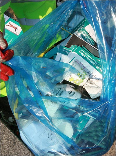 한 환경미화원이 노무현 전 대통령의 사진이 실린 주간지와 각종 물품들을 쓰레기 봉투에 담고 있다.