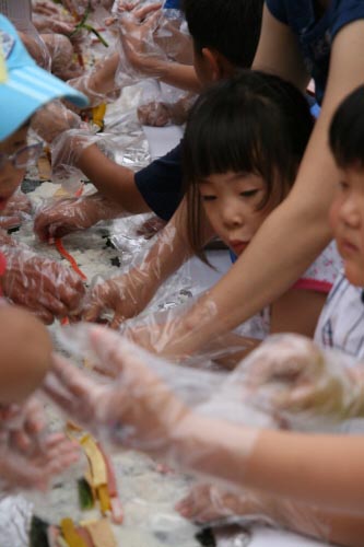 김밥을 만드는 많은 손들 사이로 얼굴을 내민 어린이