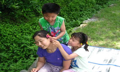 딸과 막둥이가 엄마를 꽃을 단 공주로 만들어주겠다면서 아내 귀에 꽃을 꽂아주고 있다.