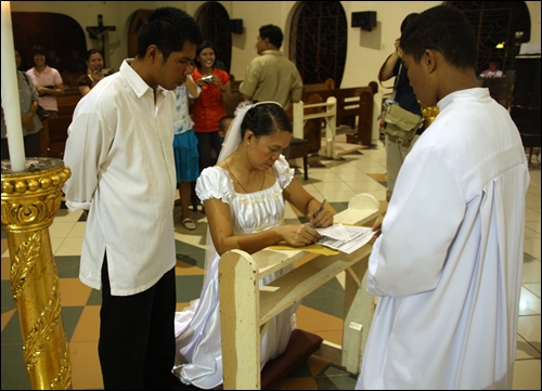 성당 신부 앞에서 혼인 서류에 서명하는 재혼 신부