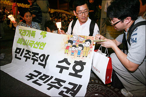 10일 저녁 서울 덕수궁 대한문 앞에서 열린 고 노무현 전 대통령 49재 추모행사에 참석한 한 가족이 '민주주의 국민주권 수호'라고 쓴 현수막을 들고 비상시국선언을 하고 있다.