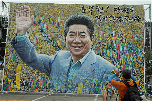 봉하마을 다목적광장에 있는 노무현 대통령의 대형 걸개그림으로, 한 사람이 휴대전화로 사진을 찍고 있다.
